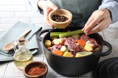 Photo of Woman preparing stew with vegetables and meat at white tiled table, closeup