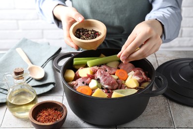 Photo of Woman preparing stew with vegetables and meat at white tiled table, closeup