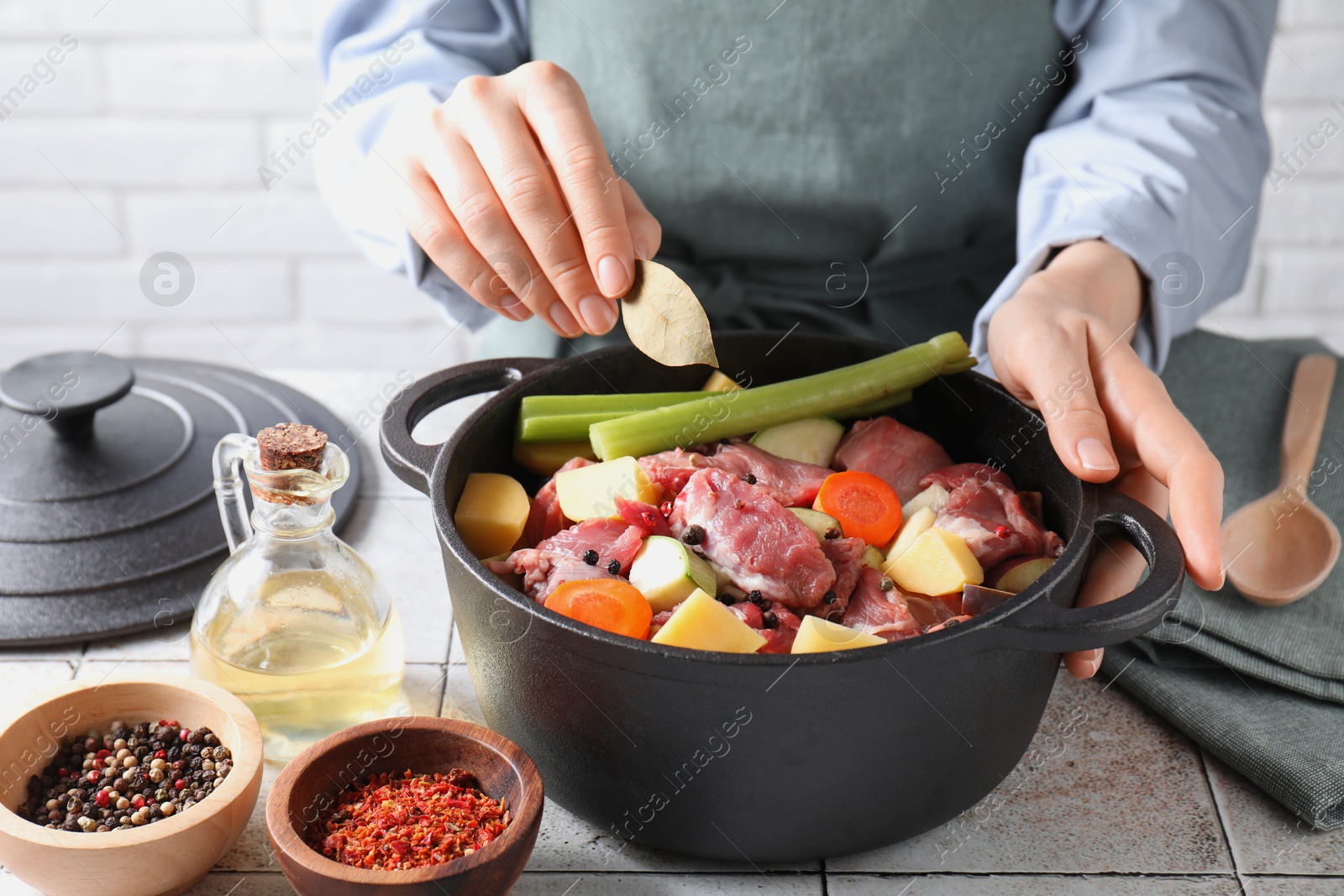 Photo of Woman preparing stew with vegetables and meat at white tiled table, closeup