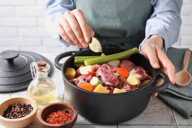 Photo of Woman preparing stew with vegetables and meat at white tiled table, closeup