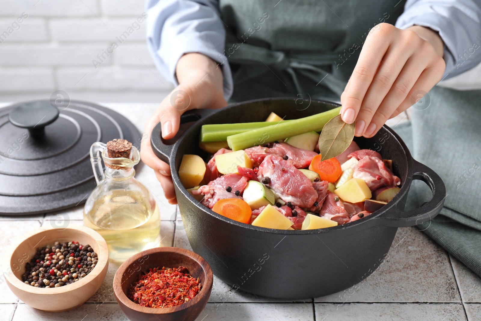 Photo of Woman preparing stew with vegetables and meat at white tiled table, closeup