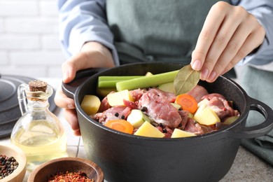 Photo of Woman preparing stew with vegetables and meat at white tiled table, closeup