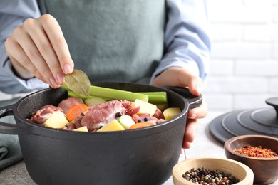 Photo of Woman preparing stew with vegetables and meat at white tiled table, closeup