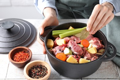 Photo of Woman preparing stew with vegetables and meat at white tiled table, closeup