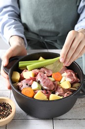 Photo of Woman preparing stew with vegetables and meat at white tiled table, closeup