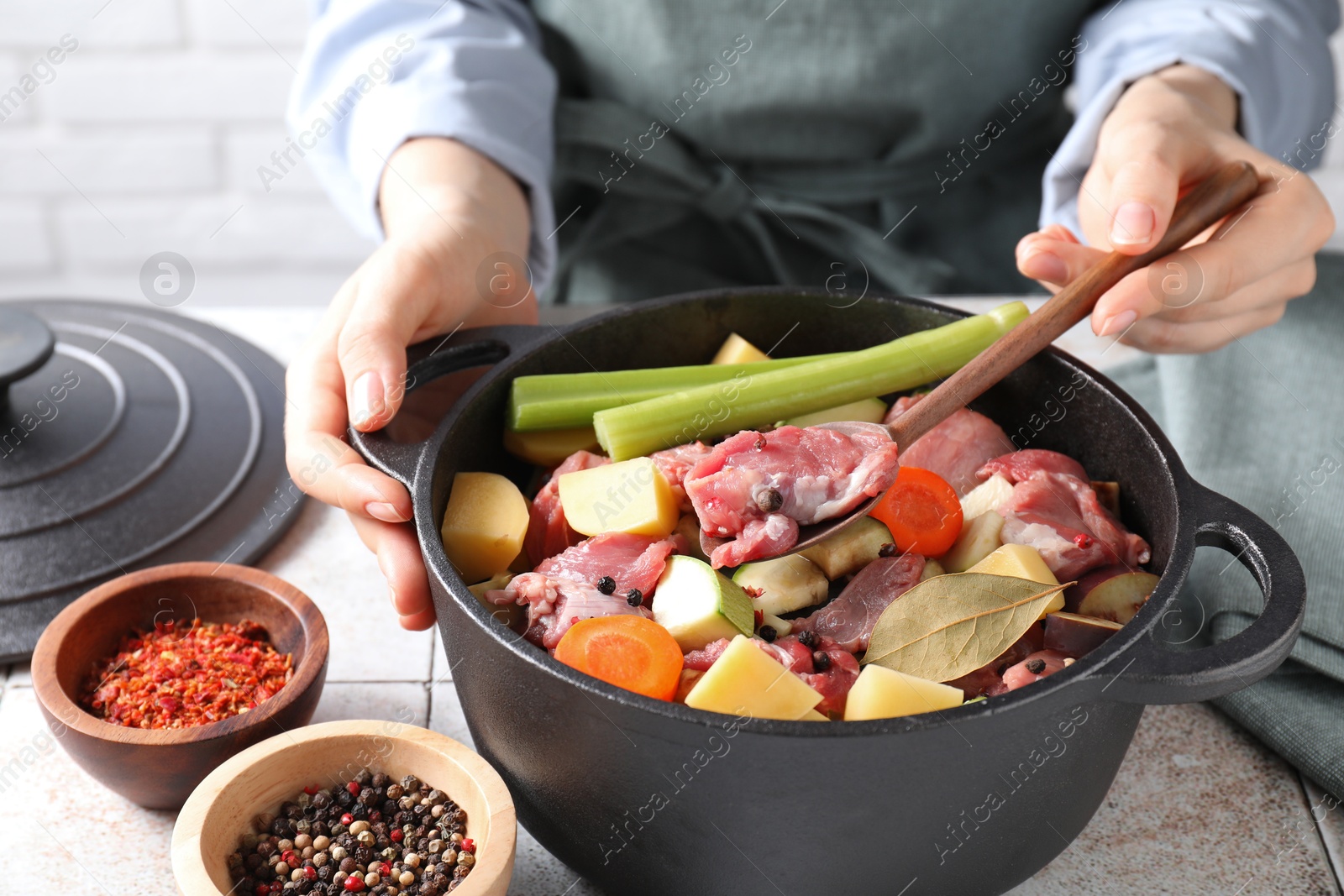 Photo of Woman preparing stew with vegetables and meat at white tiled table, closeup