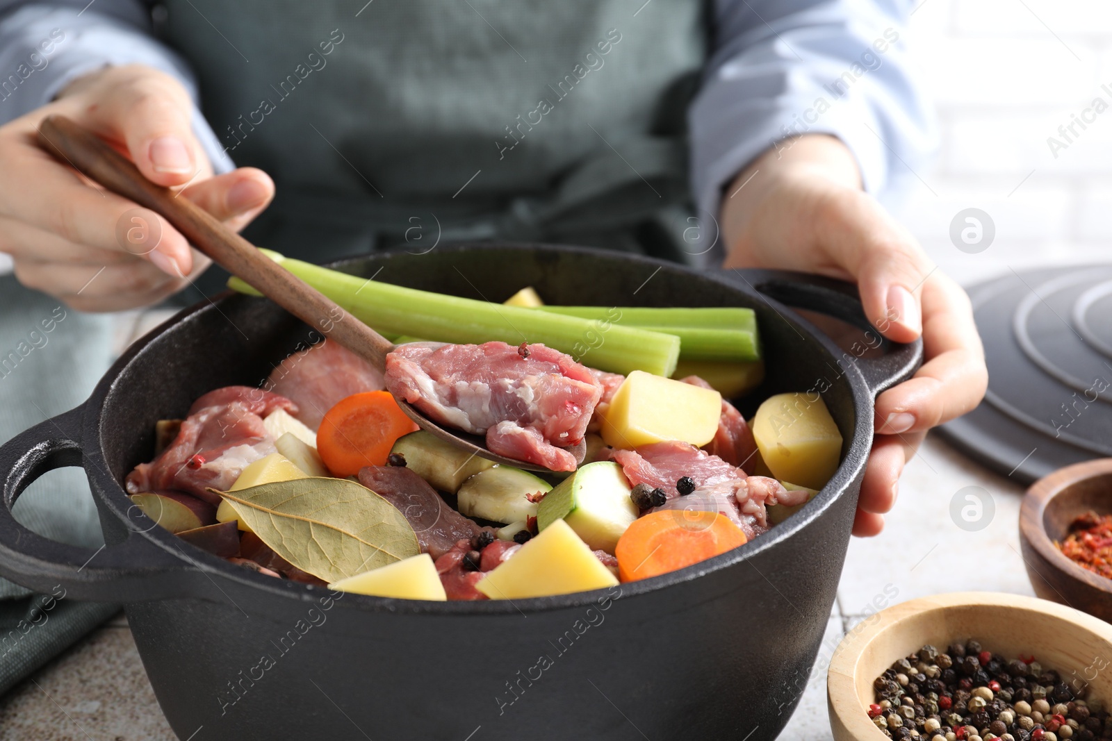 Photo of Woman preparing stew with vegetables and meat at white tiled table, closeup