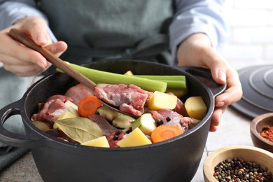 Photo of Woman preparing stew with vegetables and meat at white tiled table, closeup