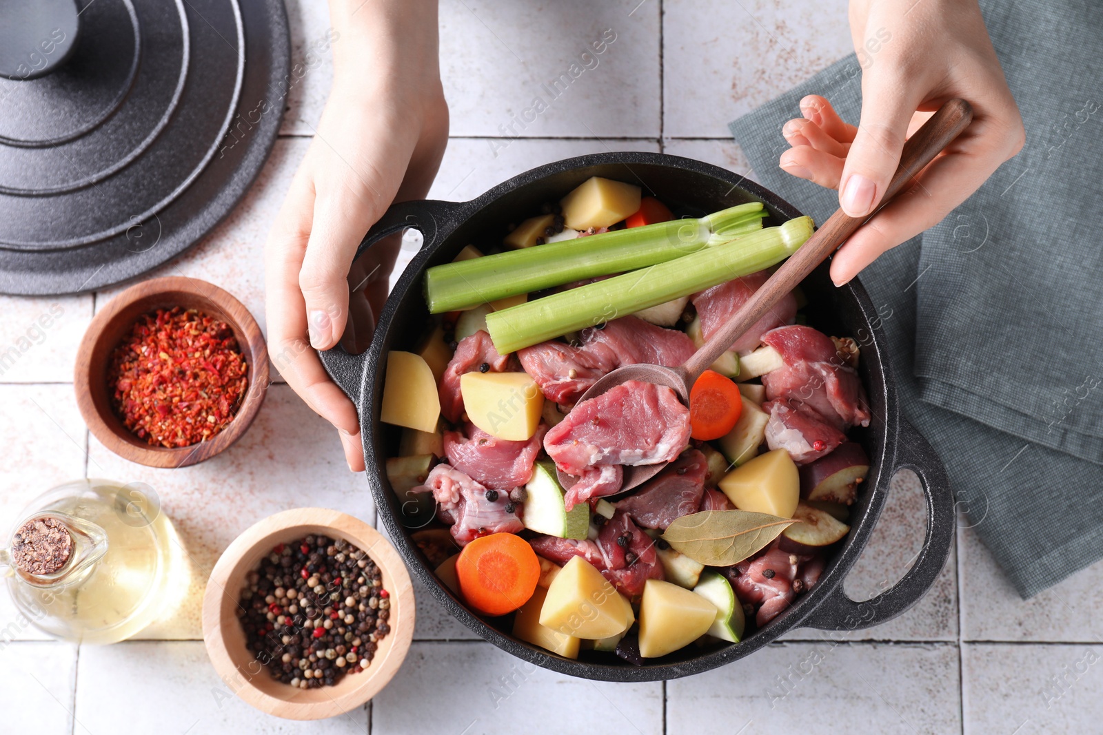 Photo of Woman preparing stew with vegetables and meat at white tiled table, top view