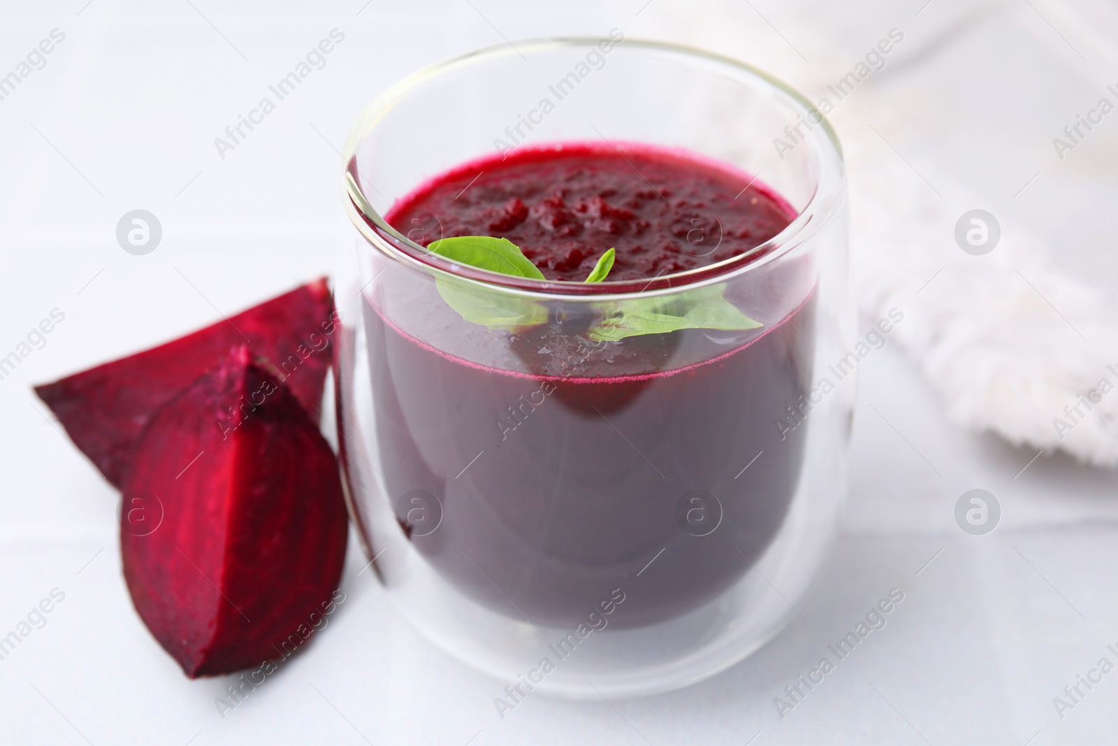 Photo of Fresh beetroot smoothie with mint in glass on white tiled table, closeup. Vegan drink