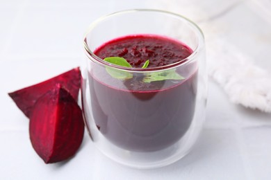 Fresh beetroot smoothie with mint in glass on white tiled table, closeup. Vegan drink