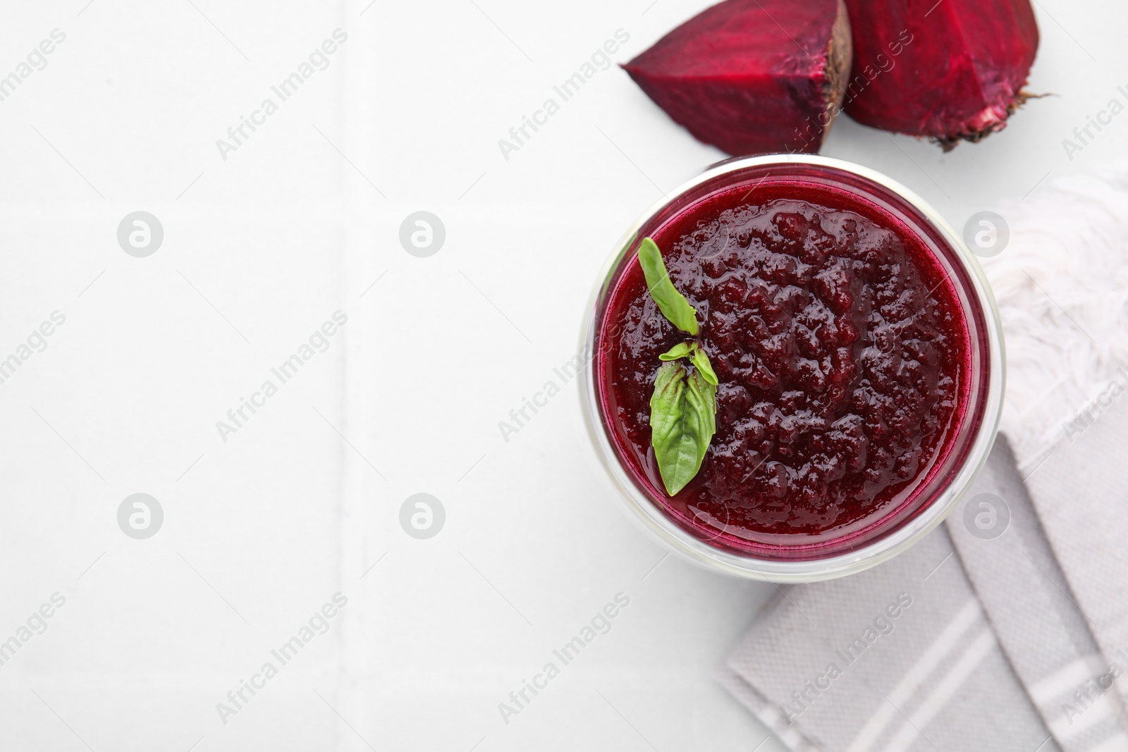 Photo of Fresh beetroot smoothie with mint in glass on white tiled table, top view. Space for text