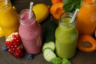 Photo of Glass bottles of tasty smoothies and different products on wooden table, closeup