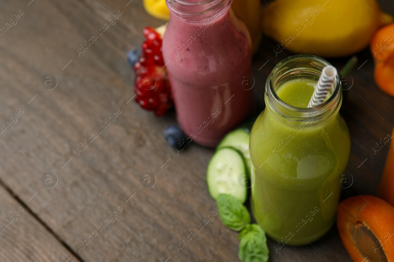 Photo of Glass bottles of tasty smoothies and different products on wooden table, closeup. Space for text