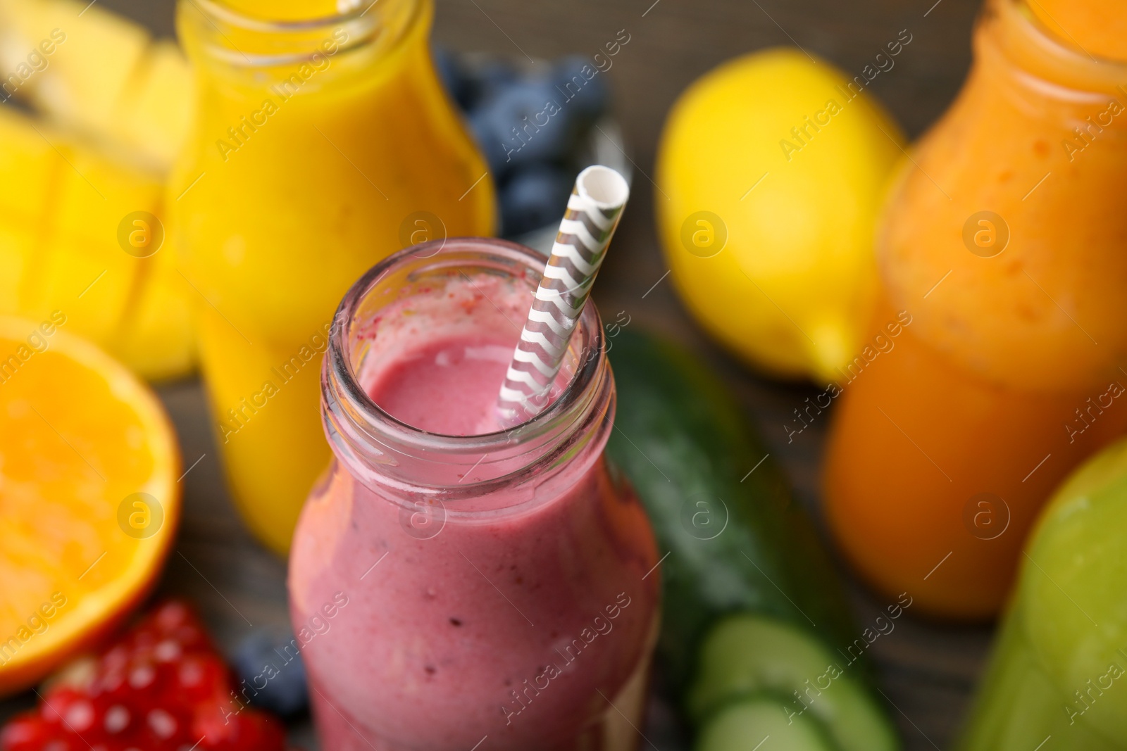 Photo of Glass bottles of tasty smoothies and different products on table, closeup