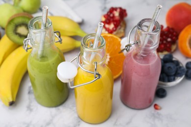 Glass bottles of tasty smoothies and different products on white marble table