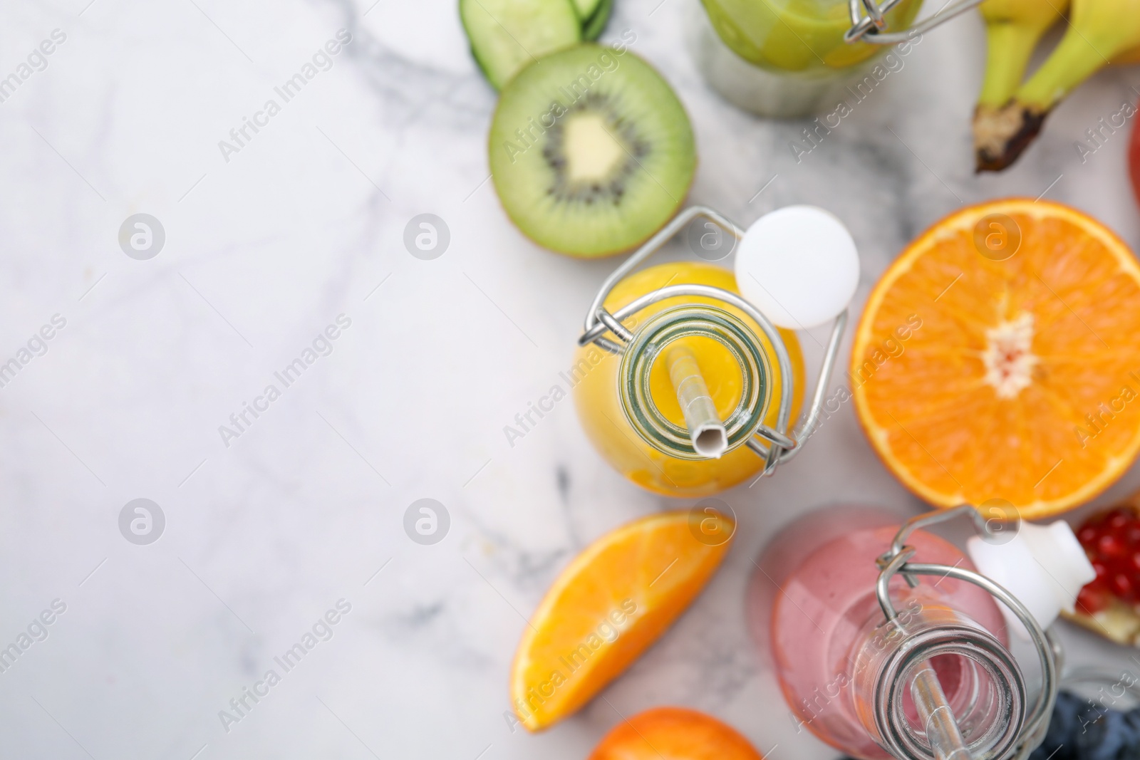 Photo of Glass bottles of tasty smoothies and different products on white marble table, flat lay. Space for text