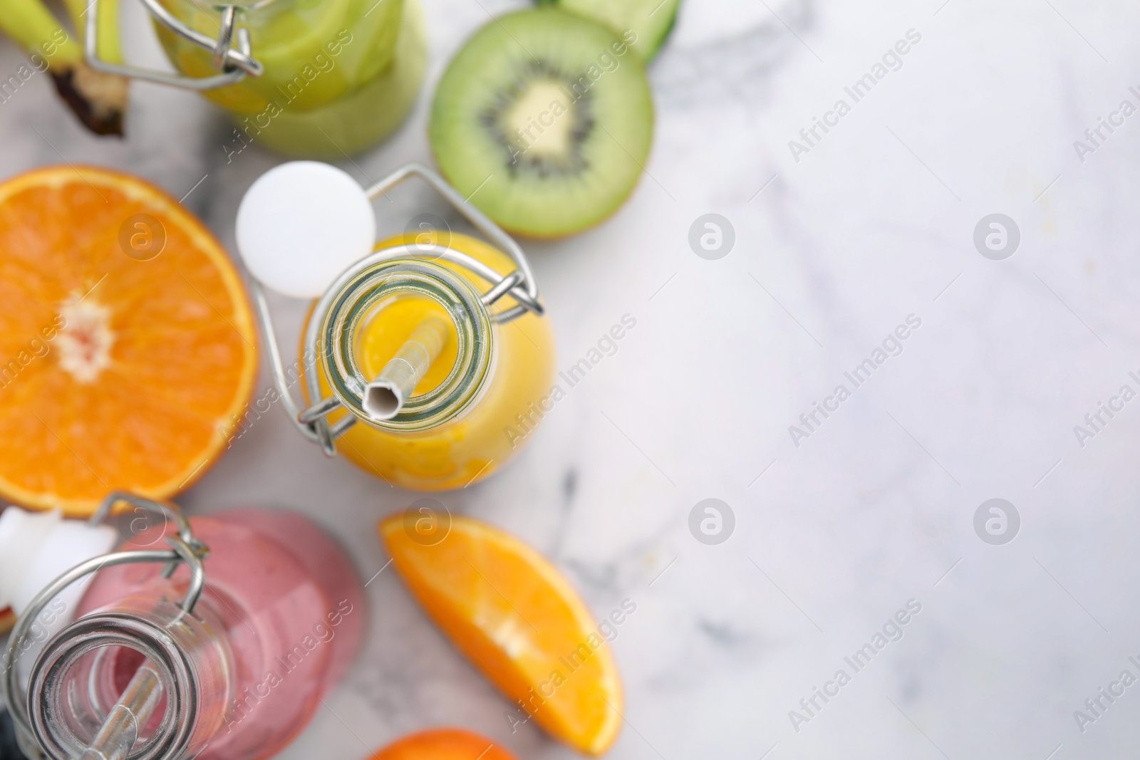 Photo of Glass bottles of tasty smoothies and different products on white marble table, flat lay. Space for text