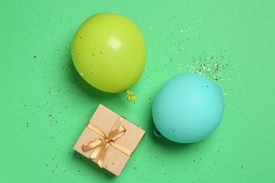 Photo of Gift box, balloons and shiny confetti on green background, flat lay