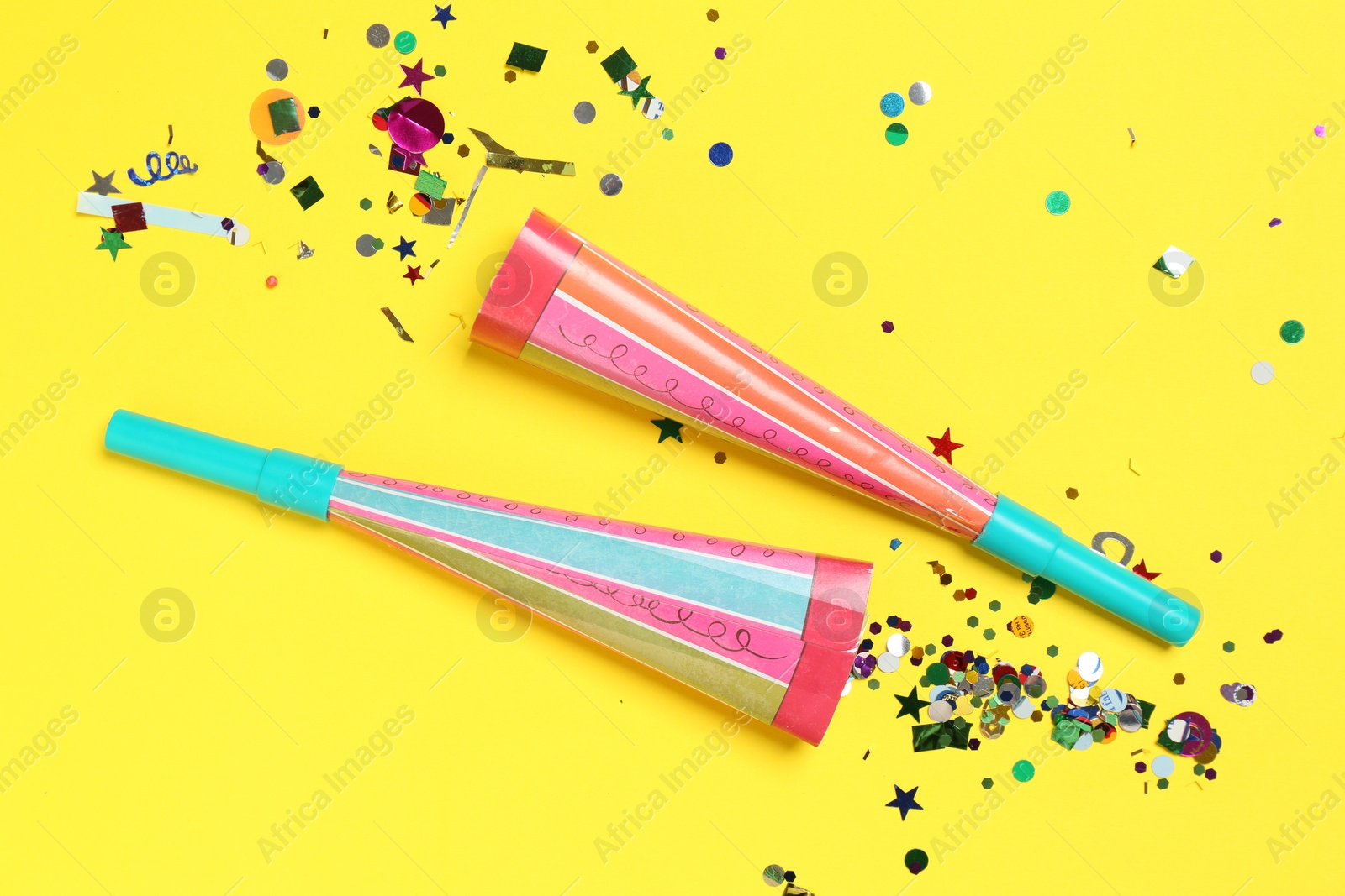 Photo of Shiny confetti and party poppers on yellow background, flat lay