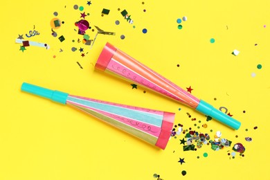 Photo of Shiny confetti and party poppers on yellow background, flat lay