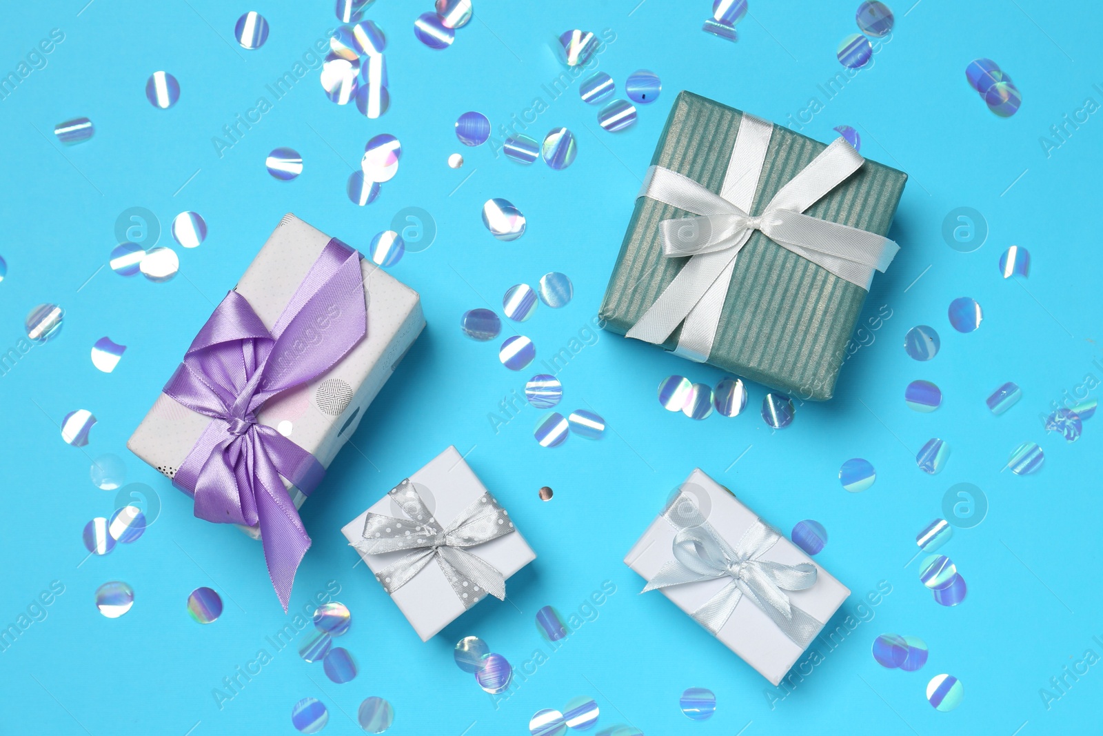 Photo of Many different gift boxes and shiny confetti on light blue background, flat lay