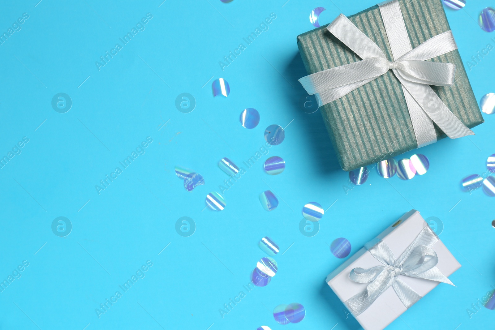 Photo of Gift boxes and shiny confetti on light blue background, flat lay. Space for text