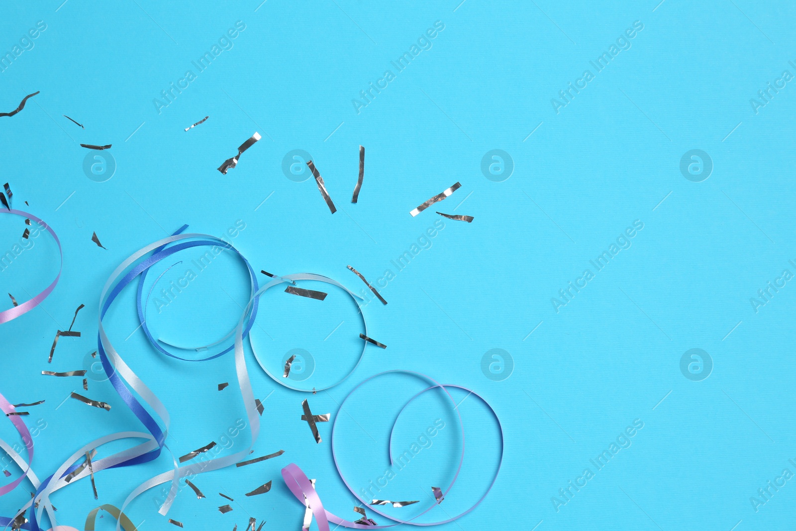 Photo of Shiny confetti and party streamers on light blue background, flat lay. Space for text