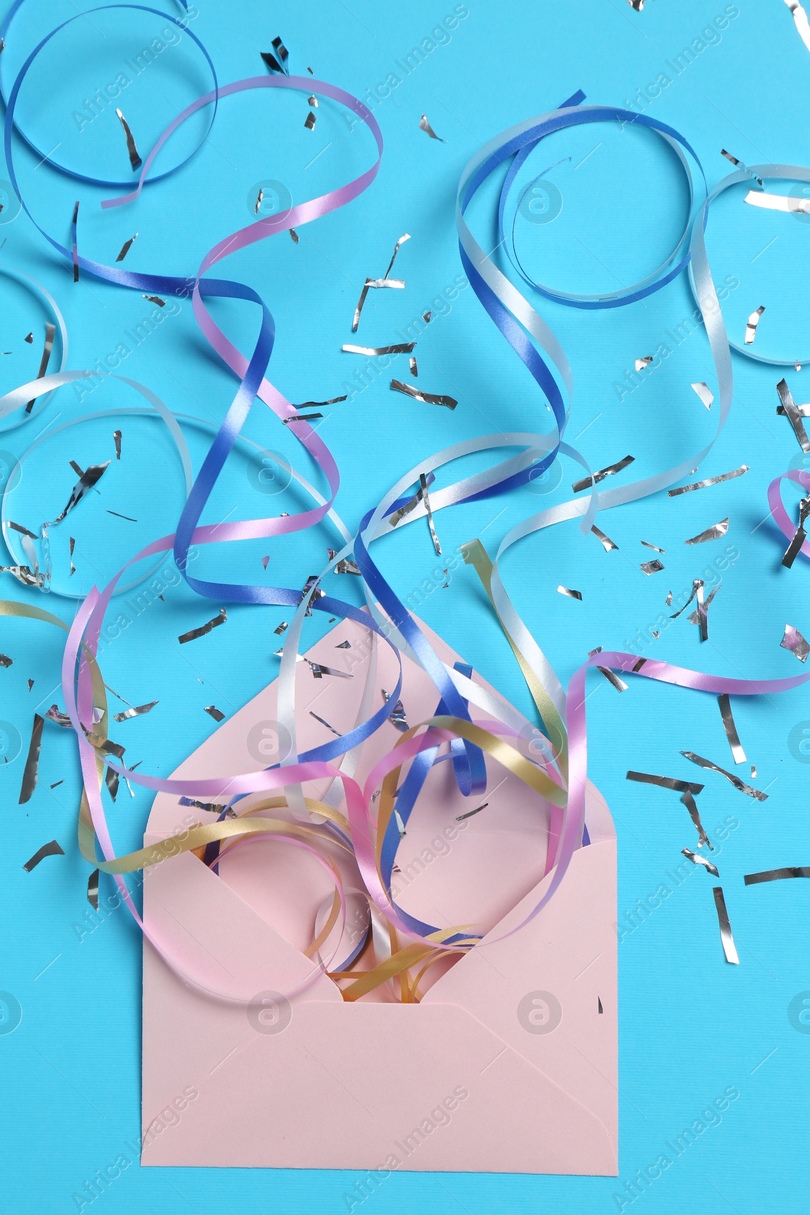 Photo of Shiny confetti and party streamers flying out of envelope on light blue background, flat lay