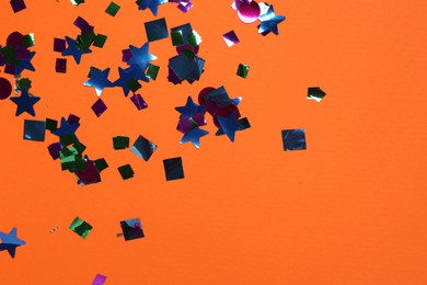 Shiny confetti on orange background, top view. Space for text