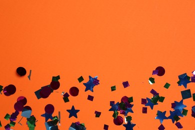 Photo of Shiny confetti on orange background, top view. Space for text