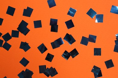 Shiny confetti on orange background, top view