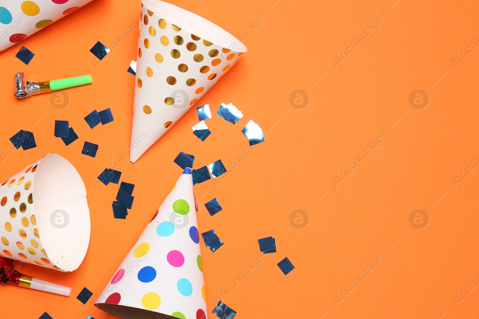 Photo of Shiny confetti, blowers and party hats on orange background, flat lay. Space for text