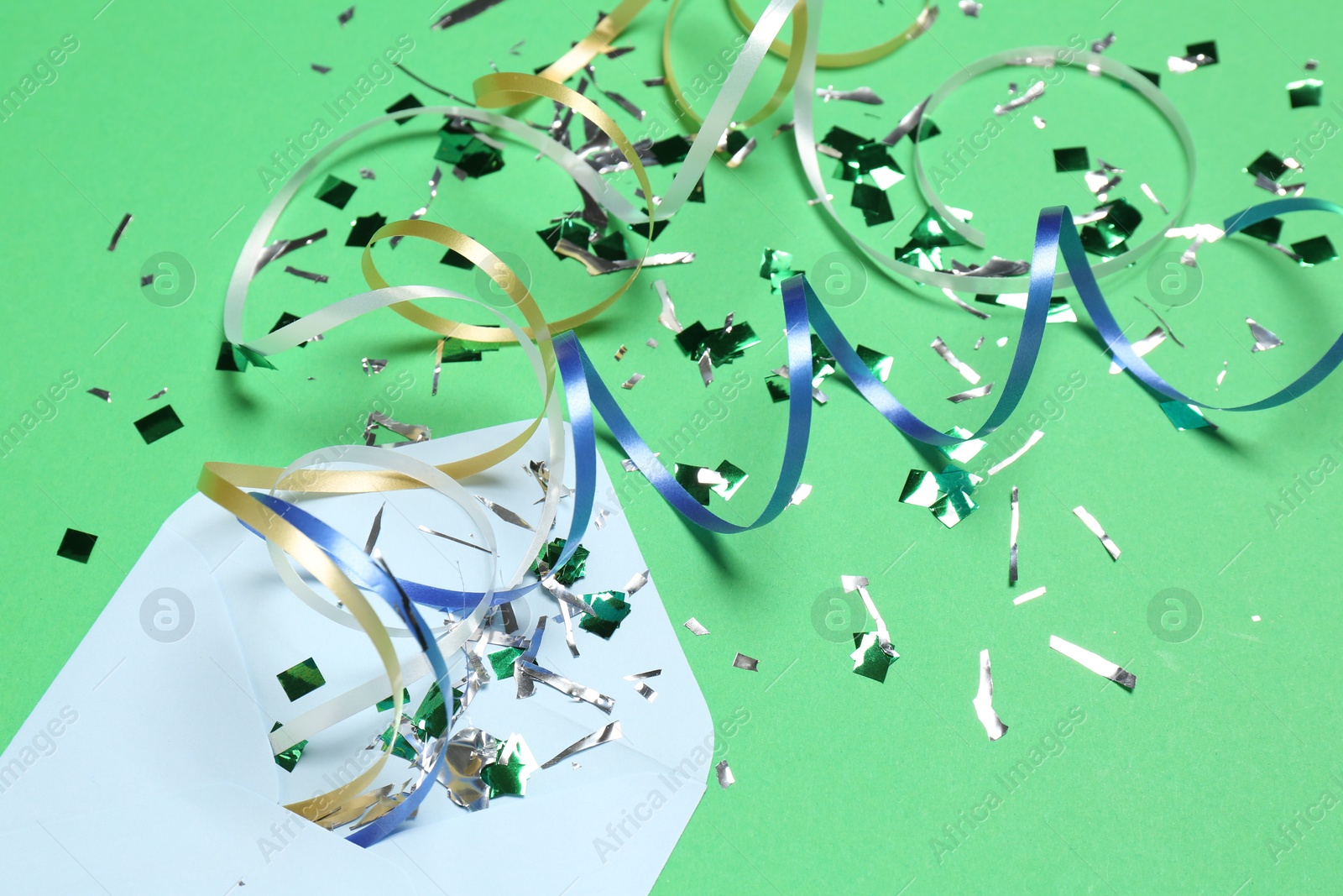 Photo of Shiny confetti, party streamers and envelope on green background, closeup