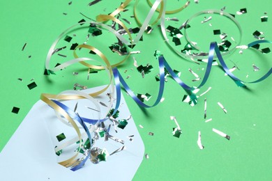 Shiny confetti, party streamers and envelope on green background, closeup