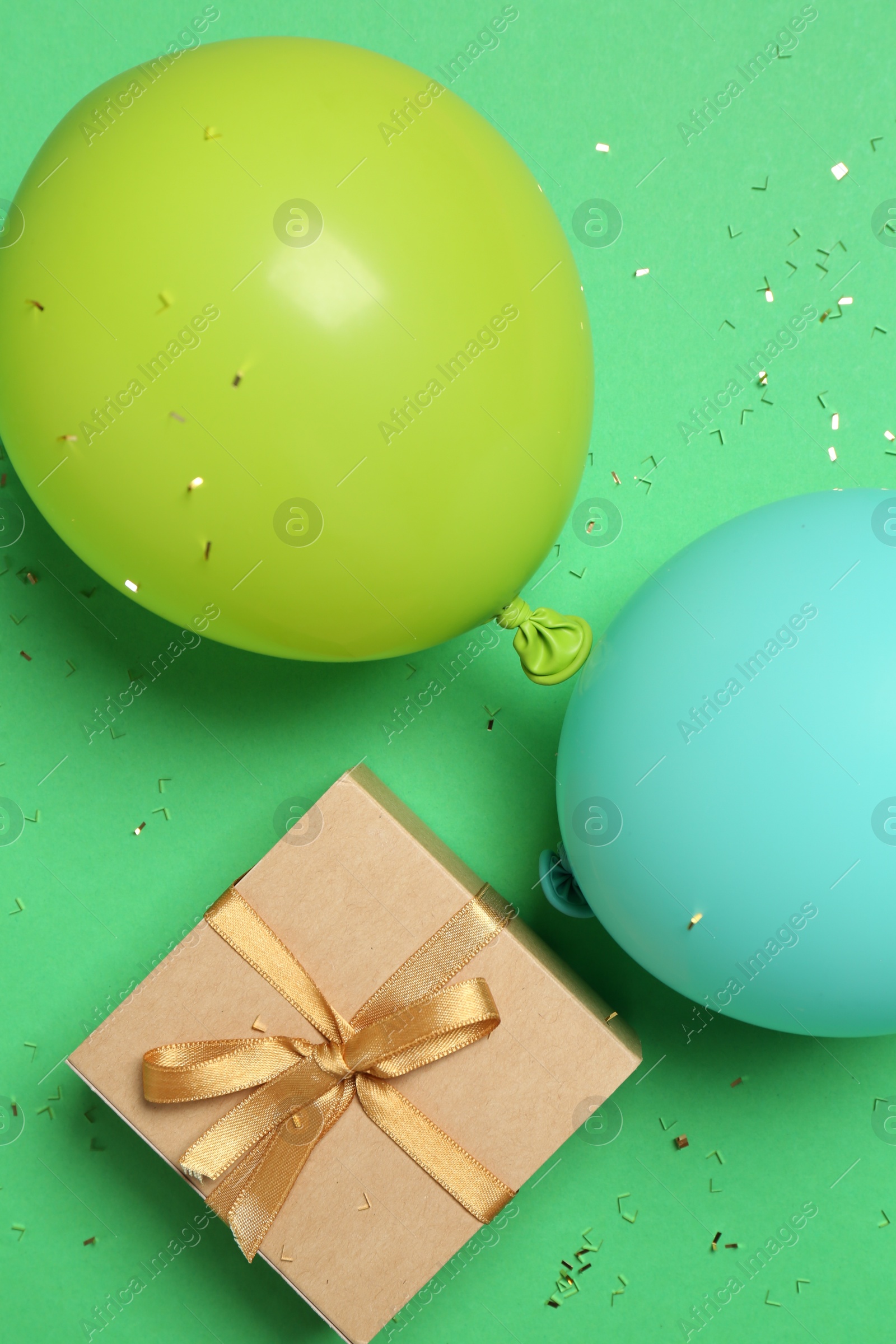 Photo of Gift box, balloons and shiny confetti on green background, flat lay