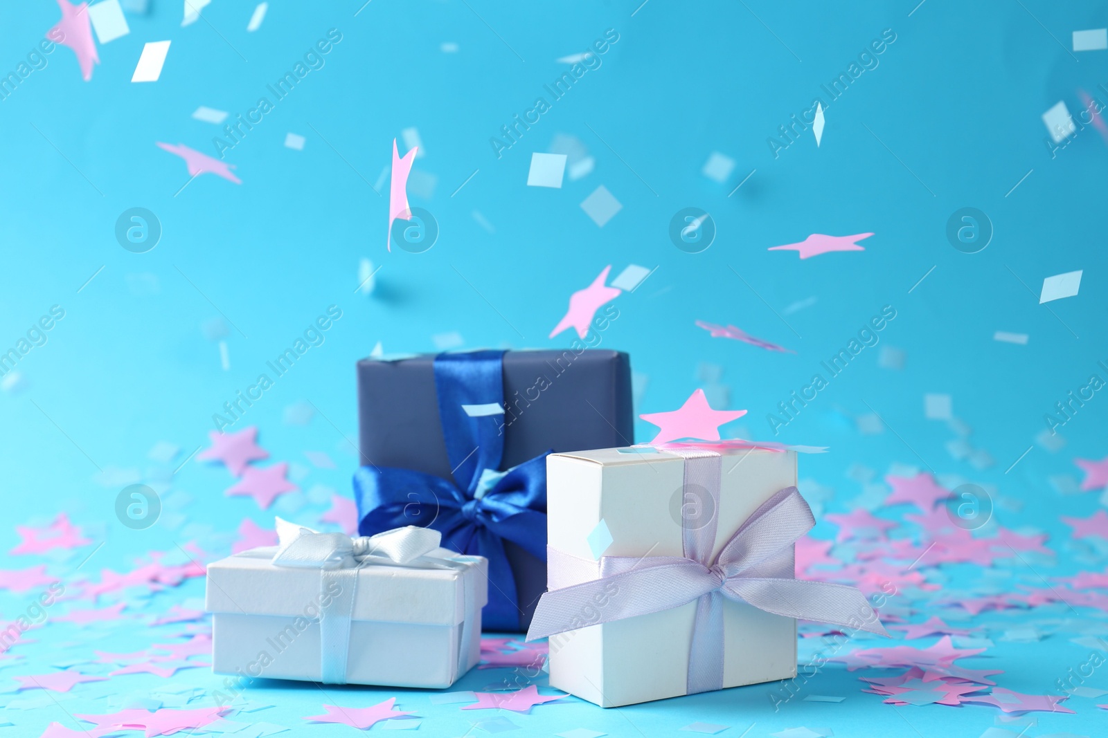 Photo of Beautiful confetti falling on gift boxes against light blue background