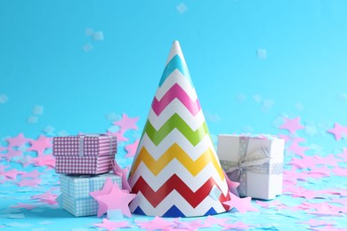 Beautiful confetti, party hat and gift boxes on light blue background, closeup