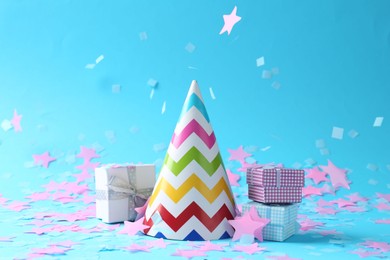 Photo of Beautiful confetti falling on party hat and gift boxes against light blue background