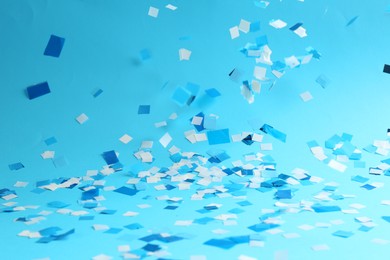 Photo of Beautiful confetti falling on light blue background, closeup