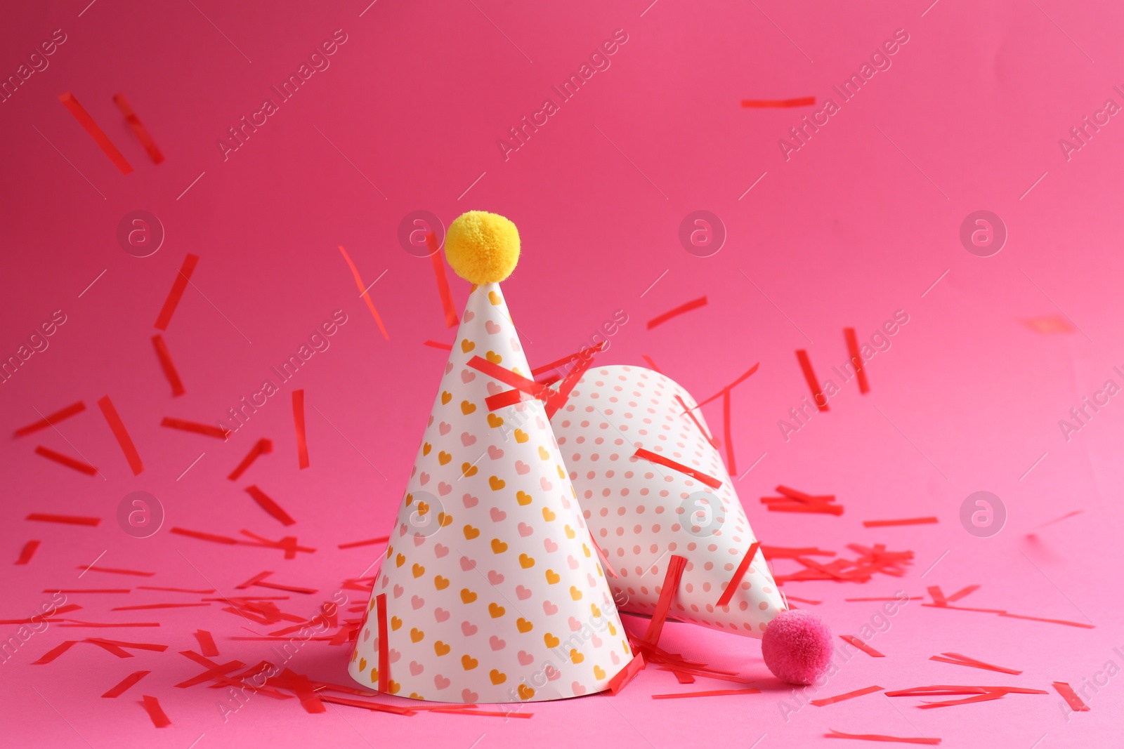 Photo of Beautiful confetti falling on party hats against pink background