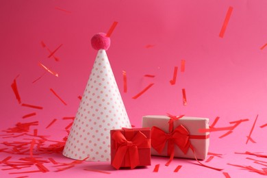 Beautiful confetti falling on party hat and gift boxes against pink background