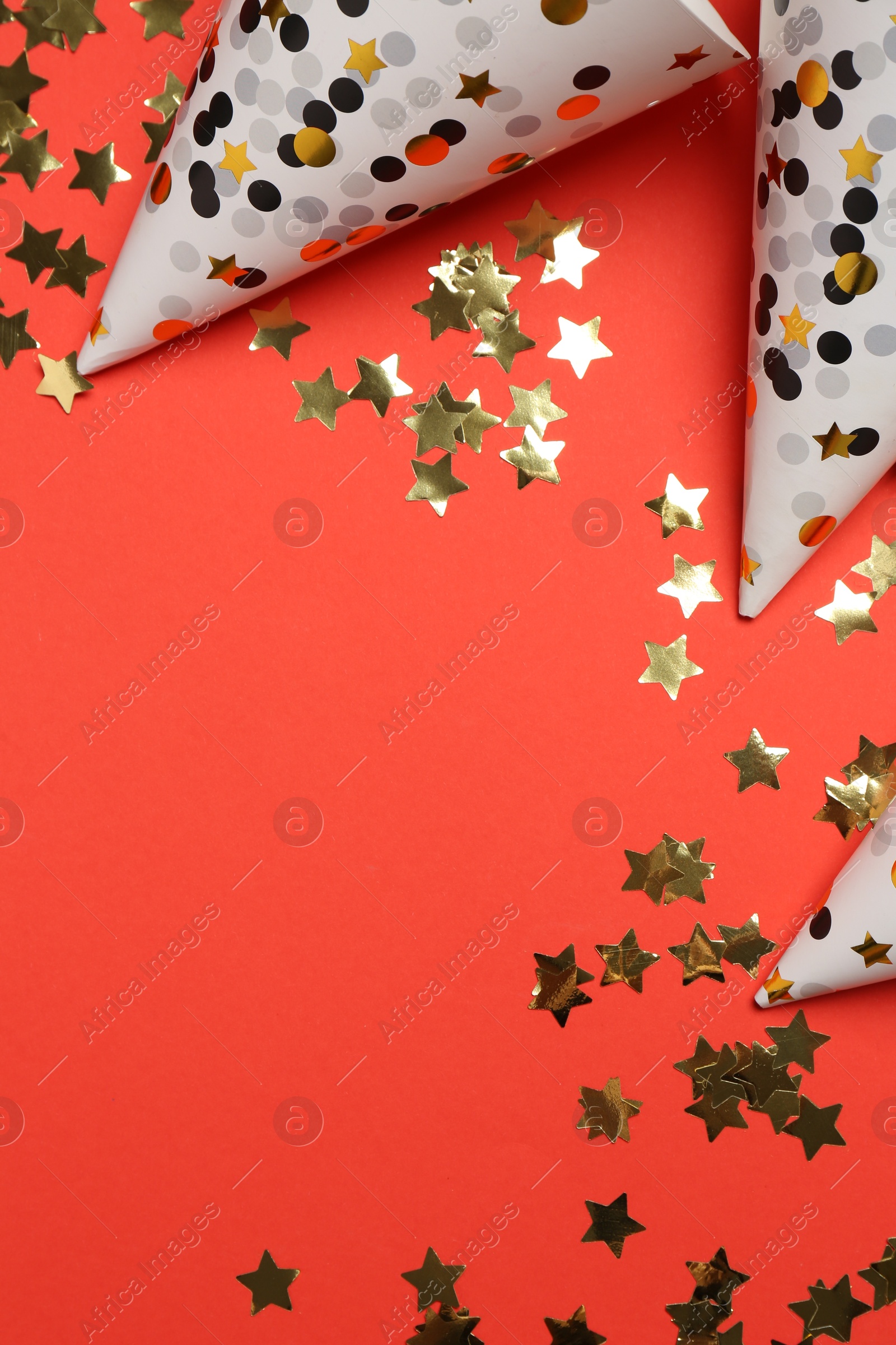 Photo of Shiny confetti and party hats on red background, flat lay. Space for text