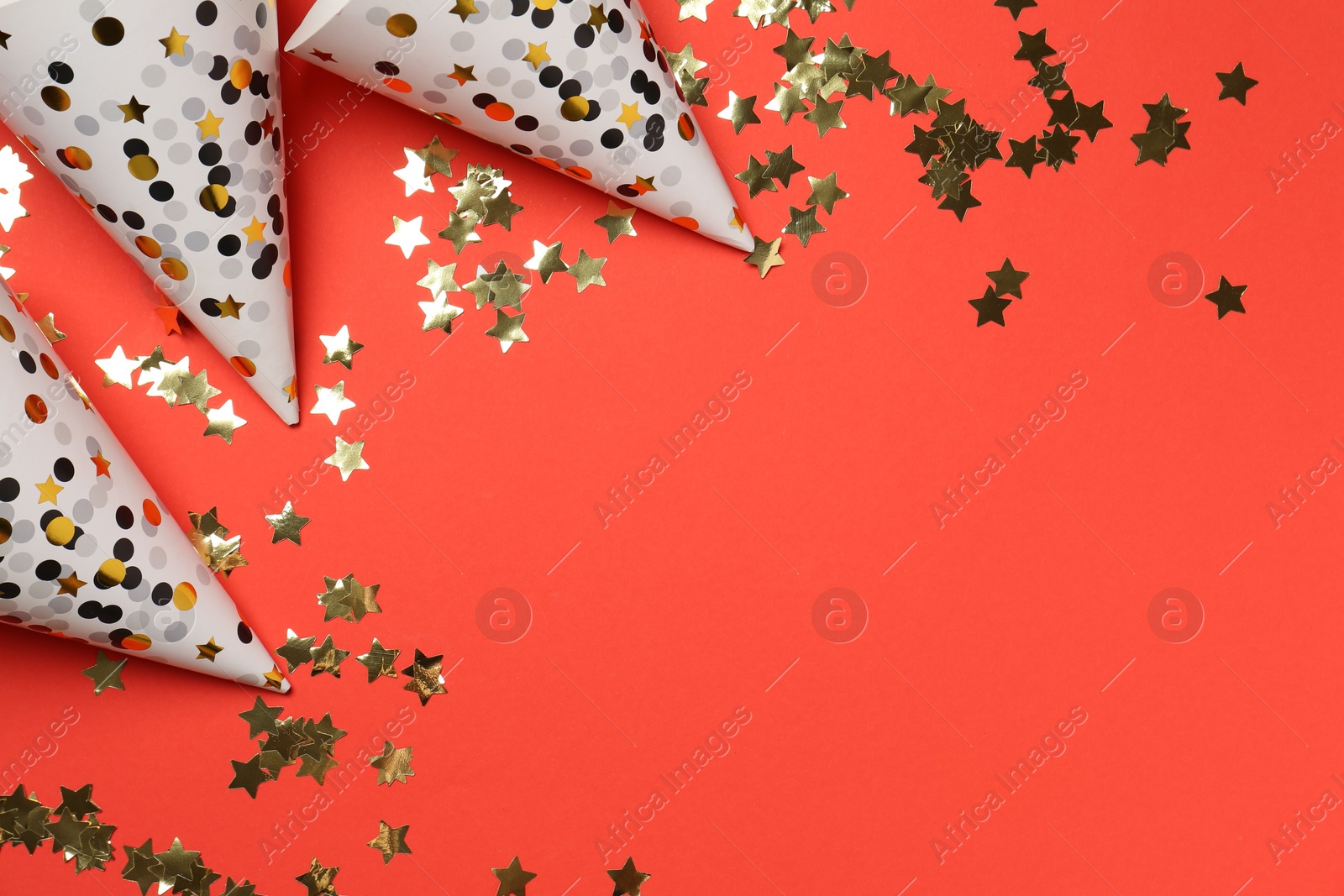 Photo of Shiny confetti and party hats on red background, flat lay. Space for text