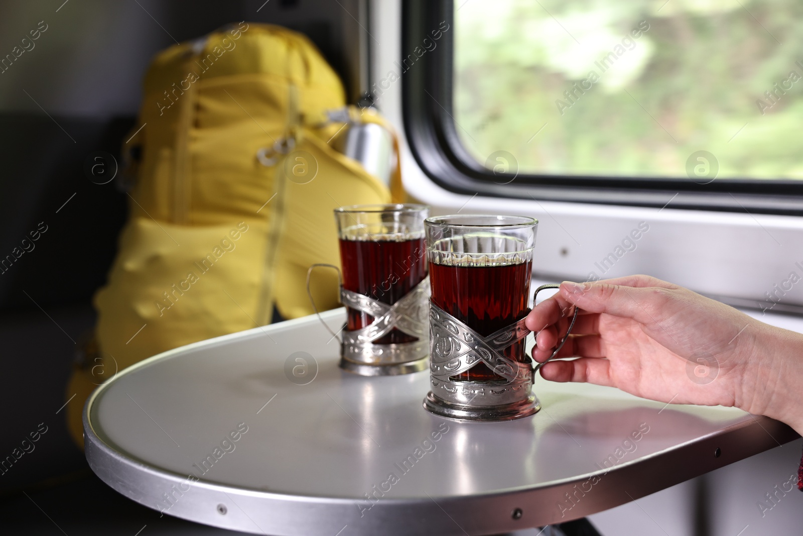 Photo of Young woman with cups of tea at table in train, closeup