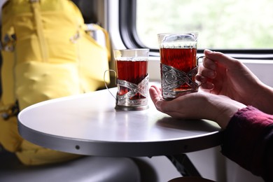 Photo of Young woman with cups of tea at table in train, closeup