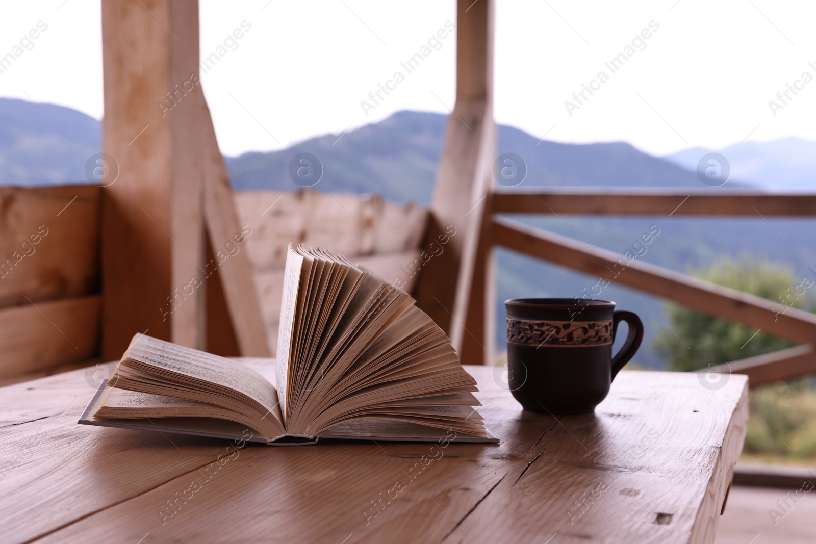 Photo of Cup of hot drink and open book on wooden table in cafe