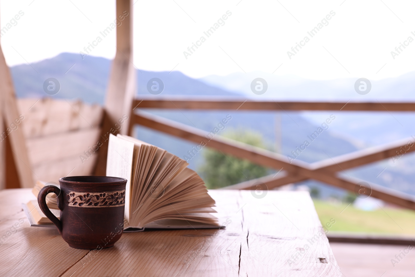 Photo of Cup of hot drink and open book on wooden table in cafe, space for text