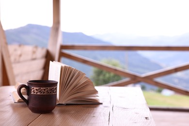 Cup of hot drink and open book on wooden table in cafe, space for text