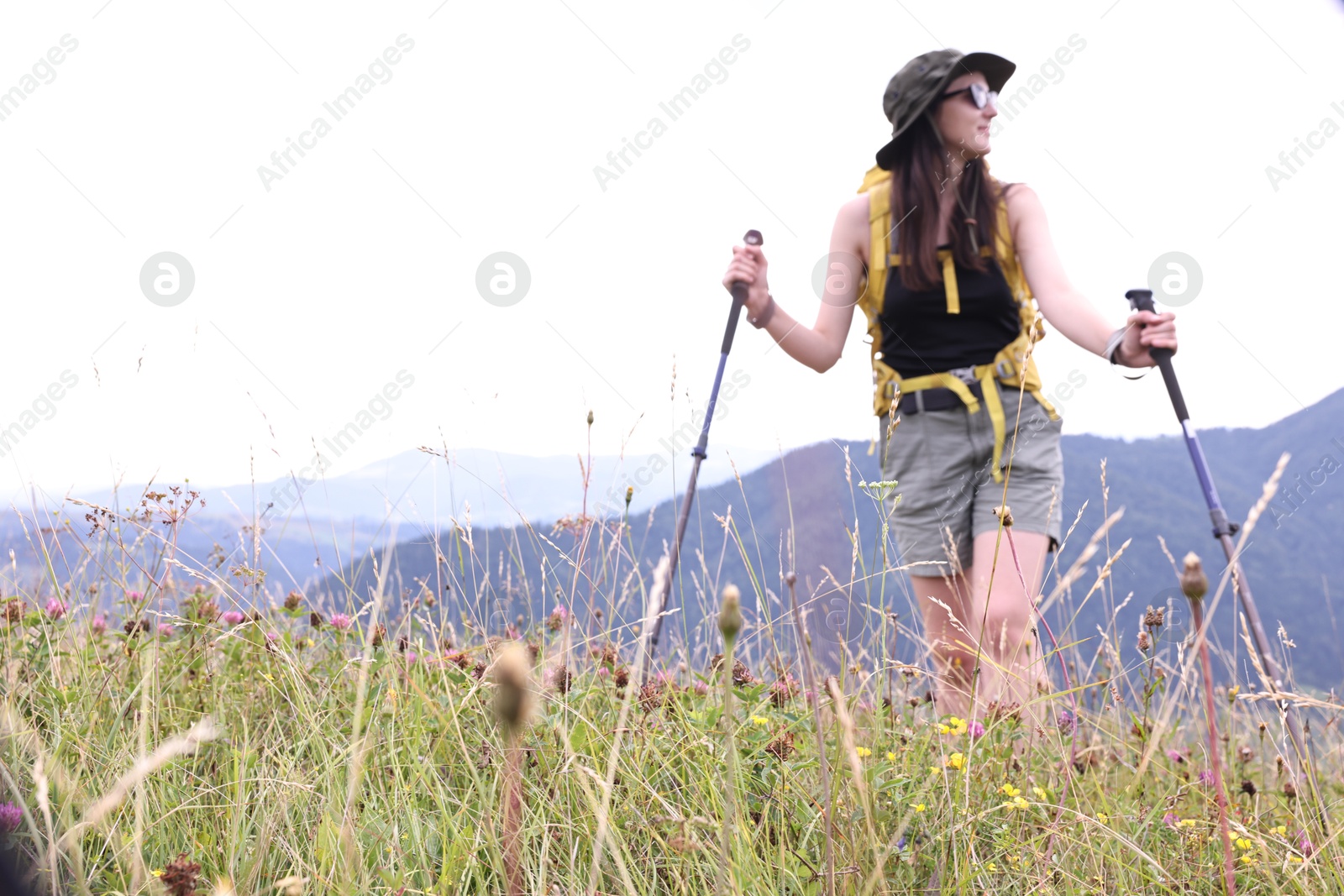 Photo of Young hiker with backpack and trekking poles in mountains, space for text